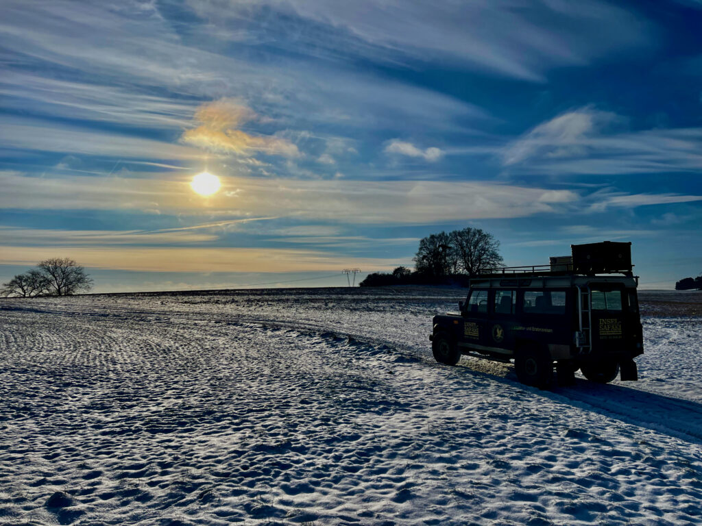 Usedom Wellness-Erlebnisse: Insel-Safari Usedom. Landrover steht auf einem Feld voller Schnee. Im Hintergrund geht die Sonne unter.