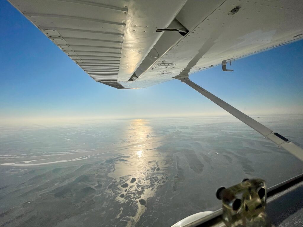Besondere Erlebnisse Usedom: Rundflug ueber Usedom mit Ostseeflug. Blick aus dem Flugzeug ueber die gefrorenen Wasserflaechen im Sonnenlicht im Winter.