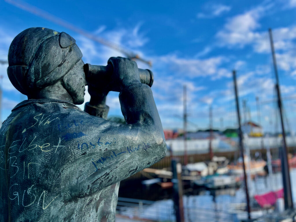 Vegesack Runde im Museumshafen Vegesack einer Bronzefigur mit Fernglas ueber die Schulter geschaut